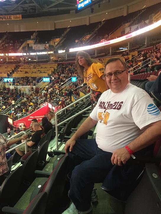 A fan wearing a team shirt sits in a crowded arena, excited for the upcoming event.