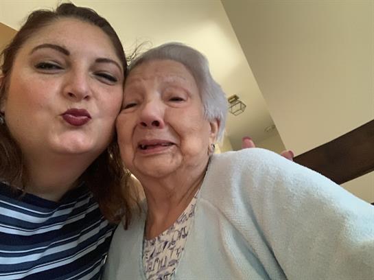 A joyful woman takes a selfie with her elderly relative in a warm home environment.