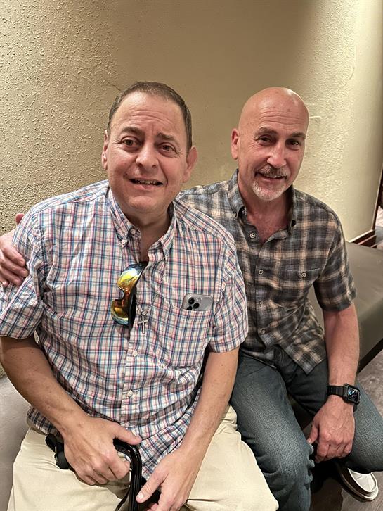Two friends sit together smiling, enjoying each other's company in a cozy indoor space.