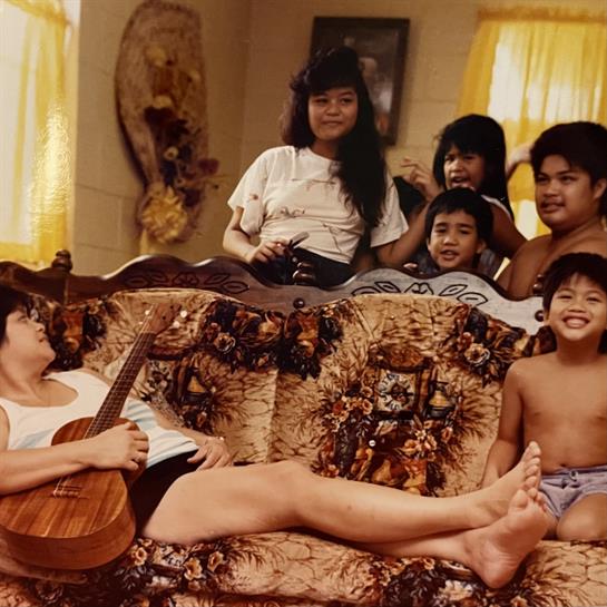 A family relaxes together in a warm living room while one person plays the guitar.