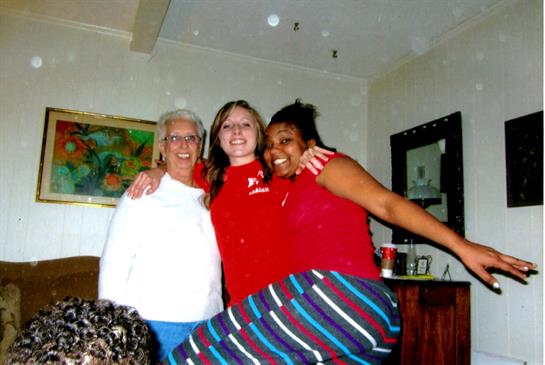 Three women pose together, smiling and enjoying their time in a welcoming living room setting.