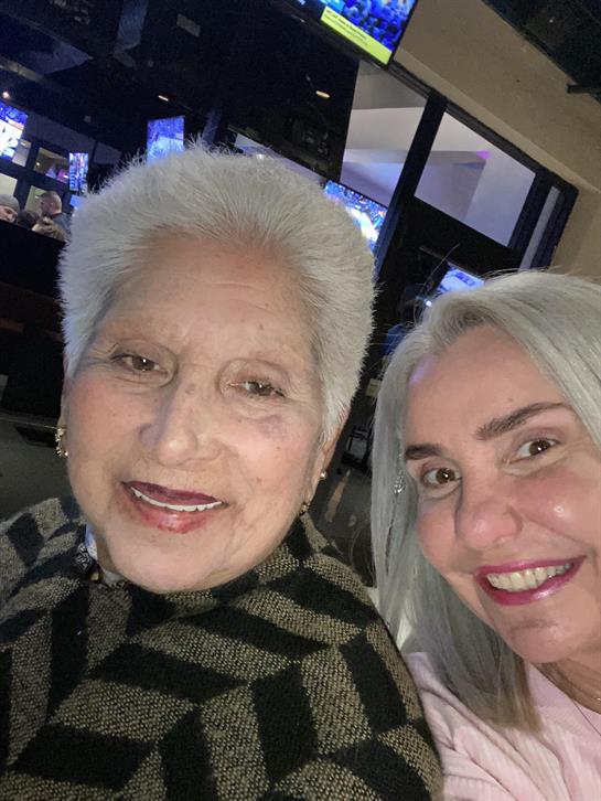 Two women are sharing smiles while seated together at a gathering with a warm atmosphere.