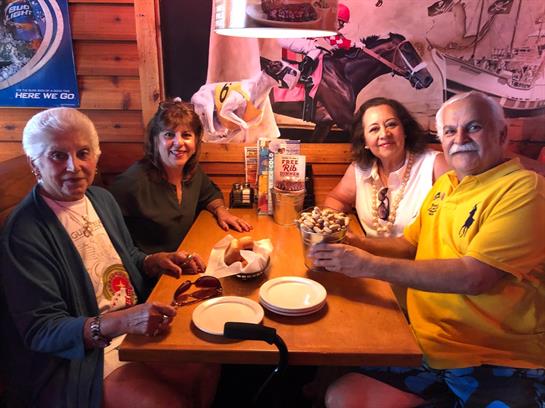 Four friends gather around a table, sharing laughter and food in a warm, inviting setting.