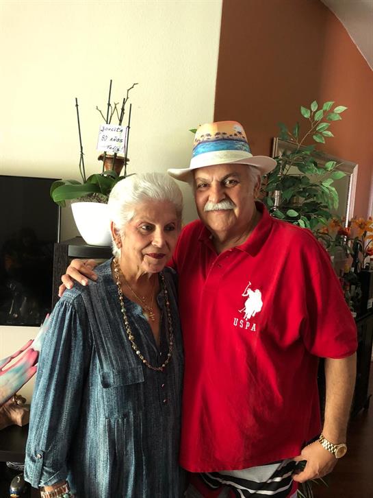 An elderly couple smiles joyfully while standing close together in a well-lit room.