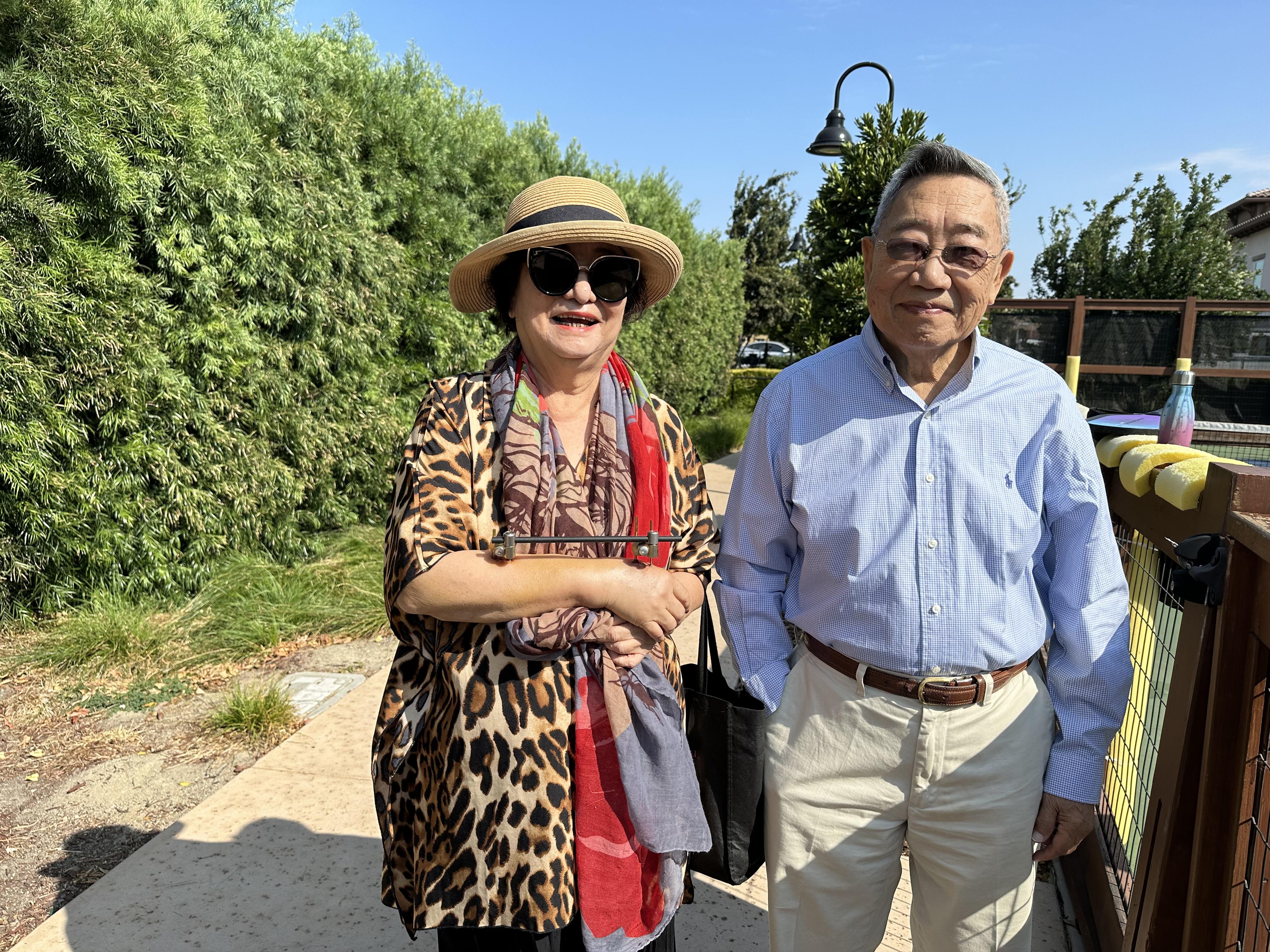An elderly couple smiles joyfully while walking together in a sunny park setting.
