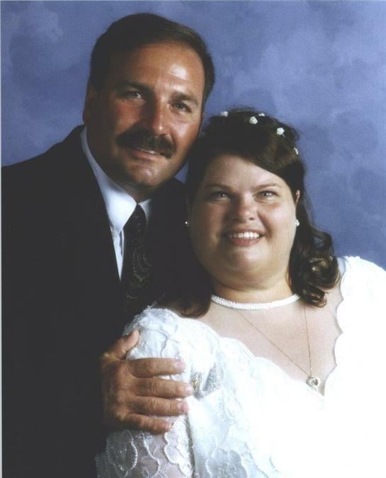 Joyful couple smiles together, showcasing their love on their wedding day against a blue backdrop.