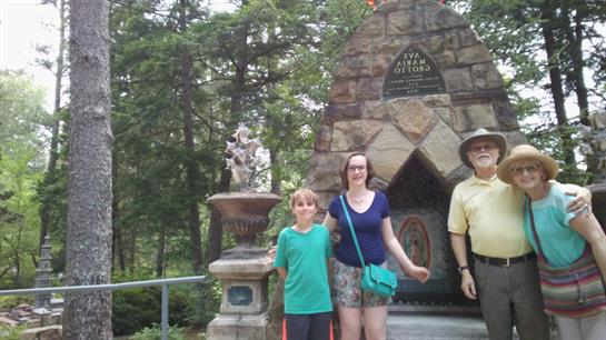 Family stands together at a historical monument amid lush greenery in a park.