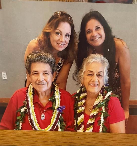 Four family members pose joyfully, adorned with colorful leis, in a cheerful restaurant atmosphere.