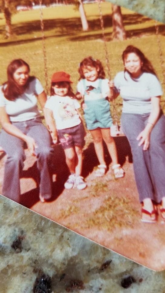 Two adults and two children enjoying a sunny day in a park, sitting on swings and smiling.