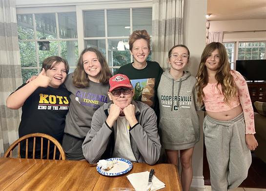 Friends gather in a warm kitchen, sharing laughs and snacks while posing happily together.