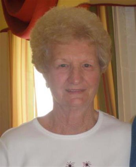 Elderly woman smiles warmly while standing near colorful curtains at home in daylight.