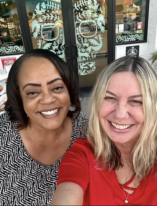 Two women are happily posing for a selfie outside a store, enjoying a friendly moment.