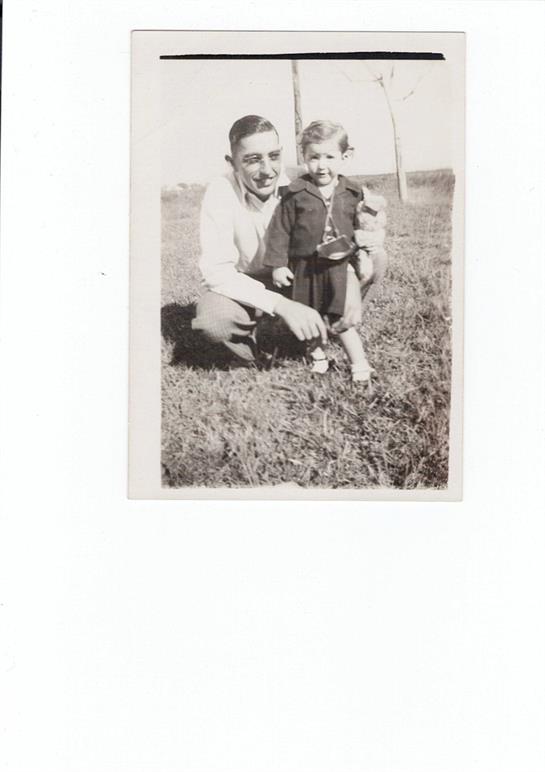 A cheerful man sits on grass with a young child, both smiling and enjoying their time together.