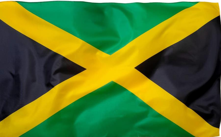 The Jamaican flag flutters energetically, showcasing its distinct colors and design against the sky.