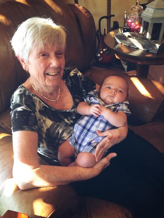 A joyful elderly woman cradles a baby in her lap, both enjoying a peaceful moment together.