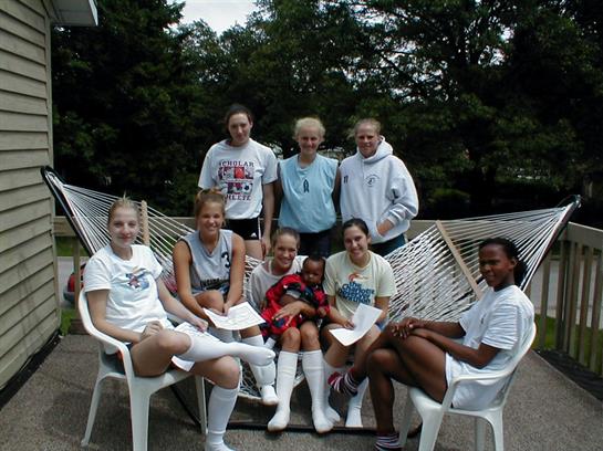 Friends relax in a backyard, seated on a hammock, sharing laughter and enjoying their time together.