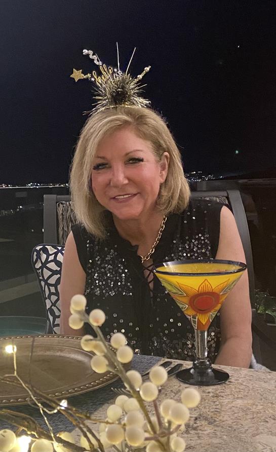 A joyful woman is celebrating while sitting outdoors with a colorful drink under the night sky.