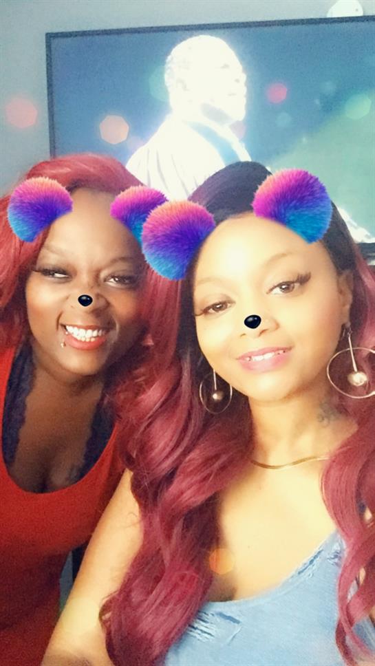 Two friends are smiling joyfully while using playful filters on a social media app together.