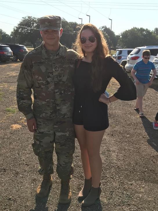 A military member poses for a picture with a young woman at a casual outdoor gathering.