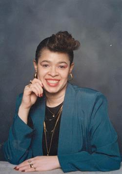 A woman with stylish hair and accessories smiles while posing elegantly.