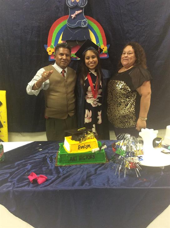 A young woman celebrates her graduation with her family beside a colorful cake and decorations.