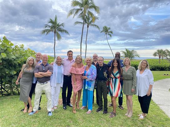 Friends gather for a joyful reunion on the lawn by the beach under a partly cloudy sky.
