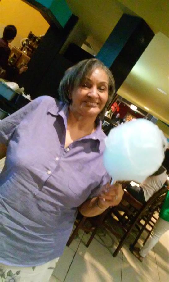 An elderly woman enjoys a large fluffy cotton candy while smiling in a lively restaurant.