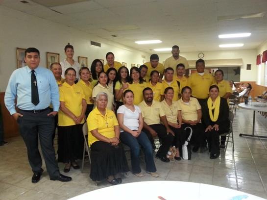 A diverse group of volunteers poses together in yellow shirts at a community gathering.