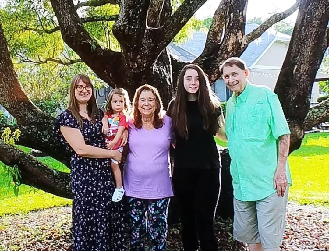 Five family members standing together outside, smiling joyfully in a sunlit backyard.