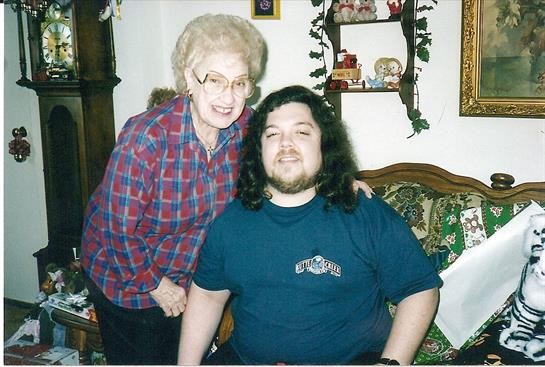 A young man with long hair smiles alongside an older woman, showcasing their bond in a warm home.