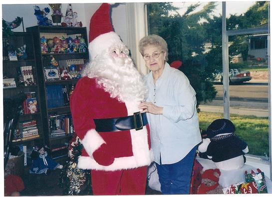 An elderly woman stands next to a life-sized Santa Claus decoration while smiling warmly.