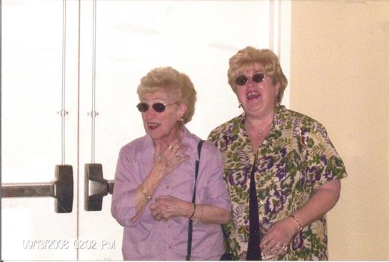 Two women, both wearing sunglasses, share a joyful moment together outdoors.