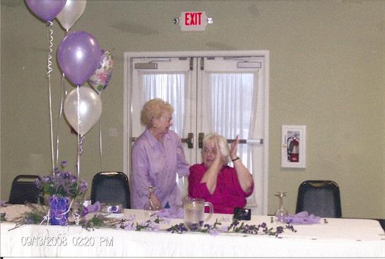 Two women enjoy a joyful moment together at a festive gathering amid purple decorations.