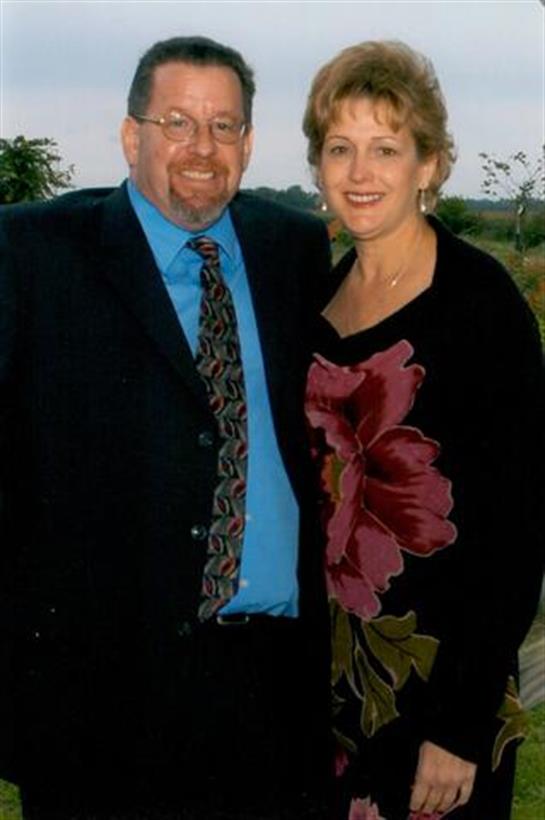 A couple stands together in a garden, dressed elegantly for a joyful celebration during dusk.