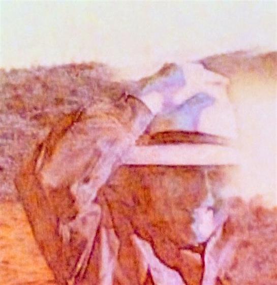 A cowboy in a wide-brimmed hat aims a gun at a target with desert hills behind him.