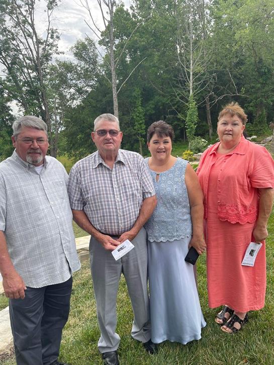 Four family members pose together outdoors, enjoying a sunny day in a natural setting.
