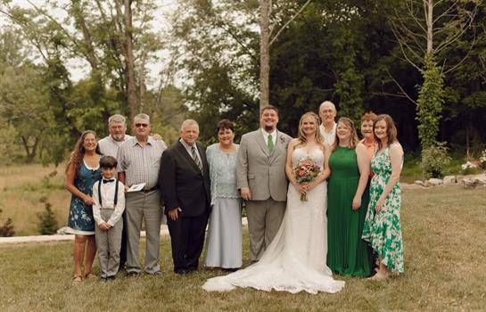 A bride stands with her family and friends in a garden, surrounded by lush greenery and smiles.