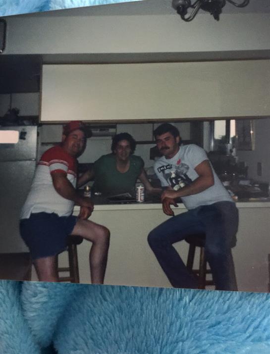 Three men relax at a kitchen bar, enjoying drinks and each other's company.