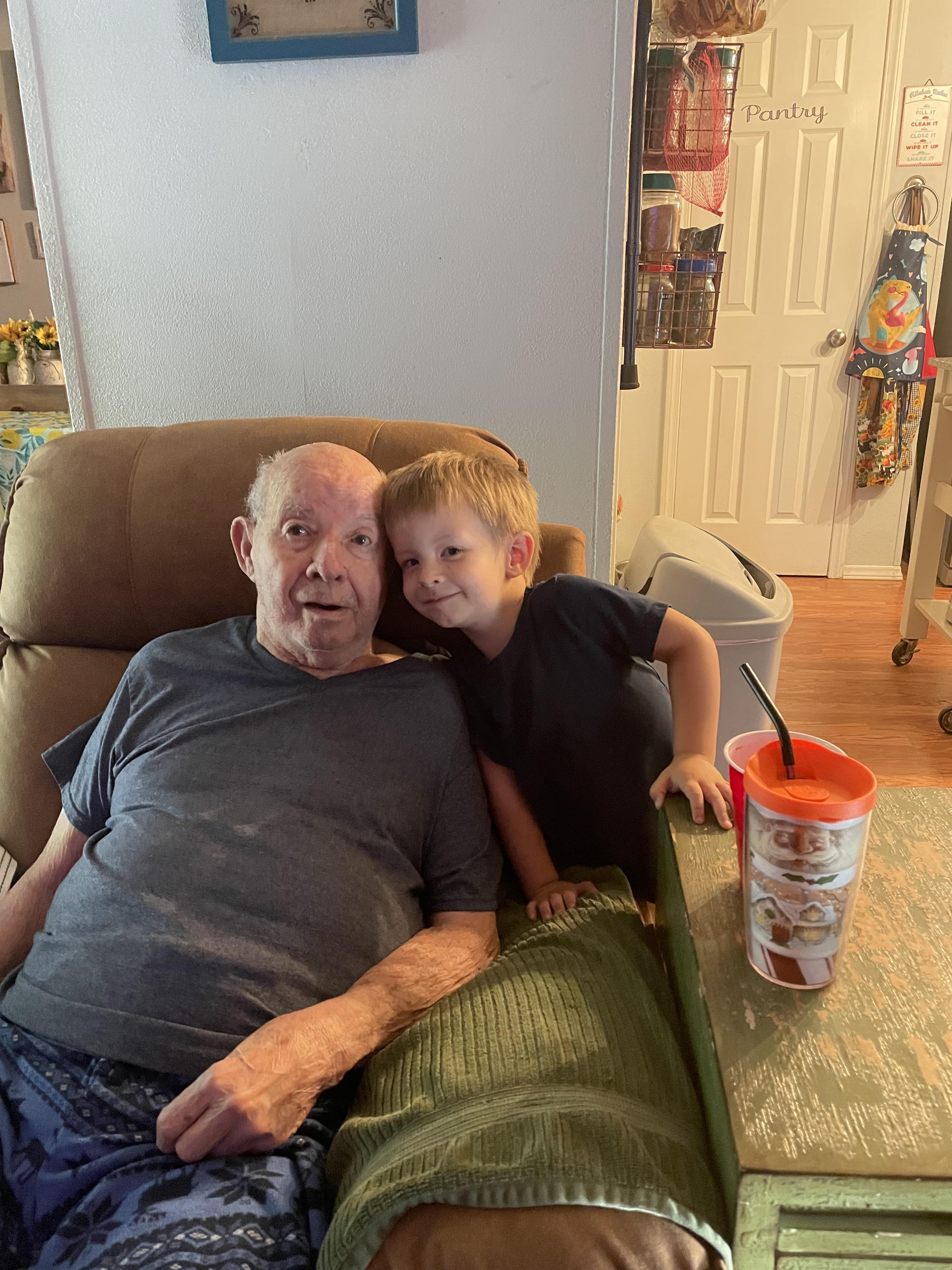 A young boy shares a warm embrace with his grandfather while seated in a cozy living room.