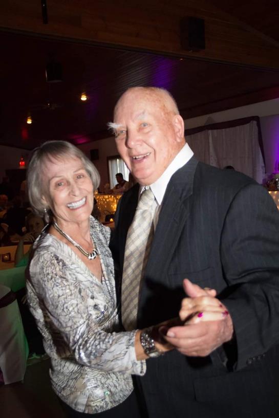 An elderly couple enjoys a lively dance at a festive gathering with vibrant lighting.