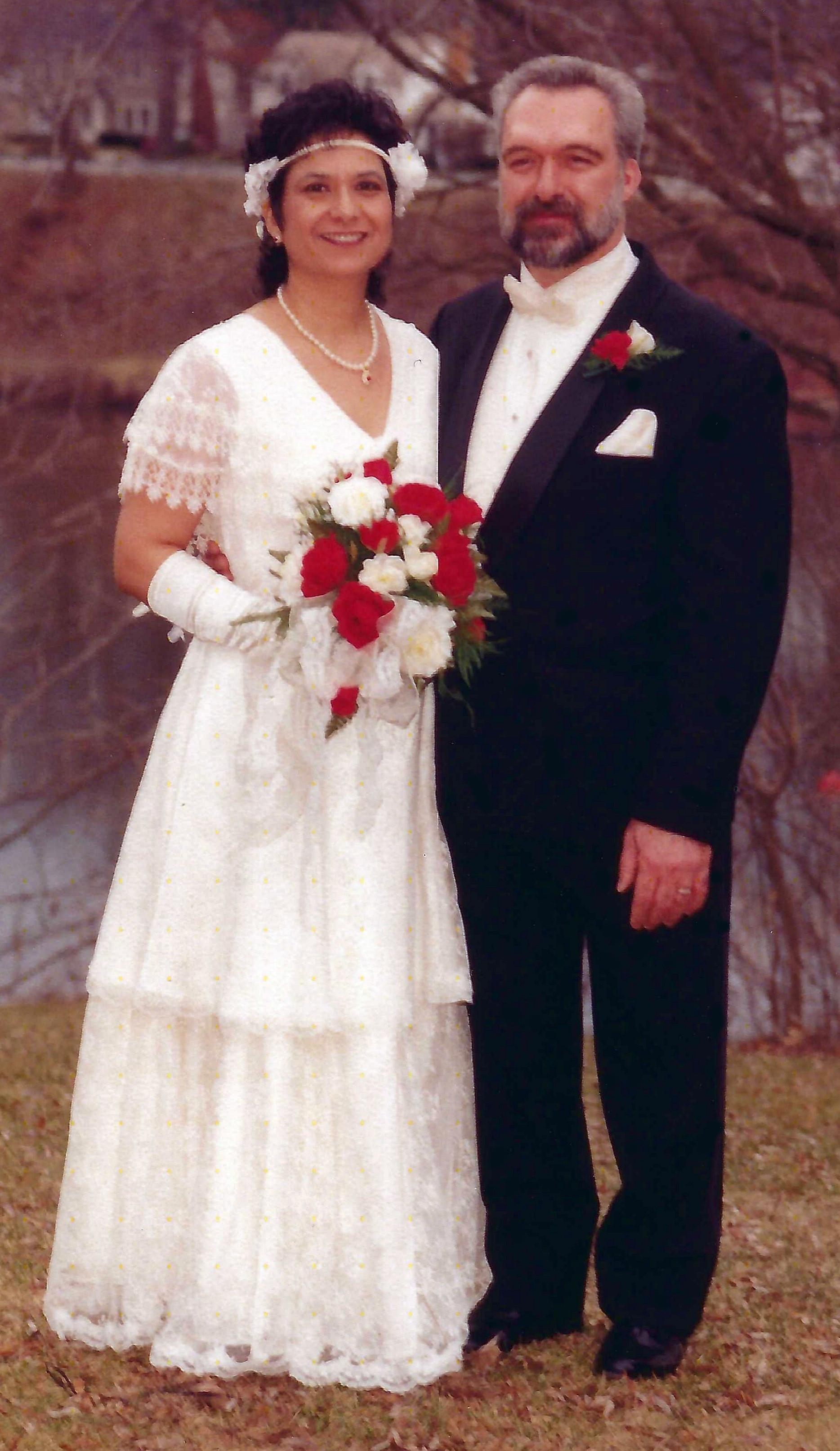 A bride and groom pose together in a lovely outdoor setting, dressed in formal wedding attire.