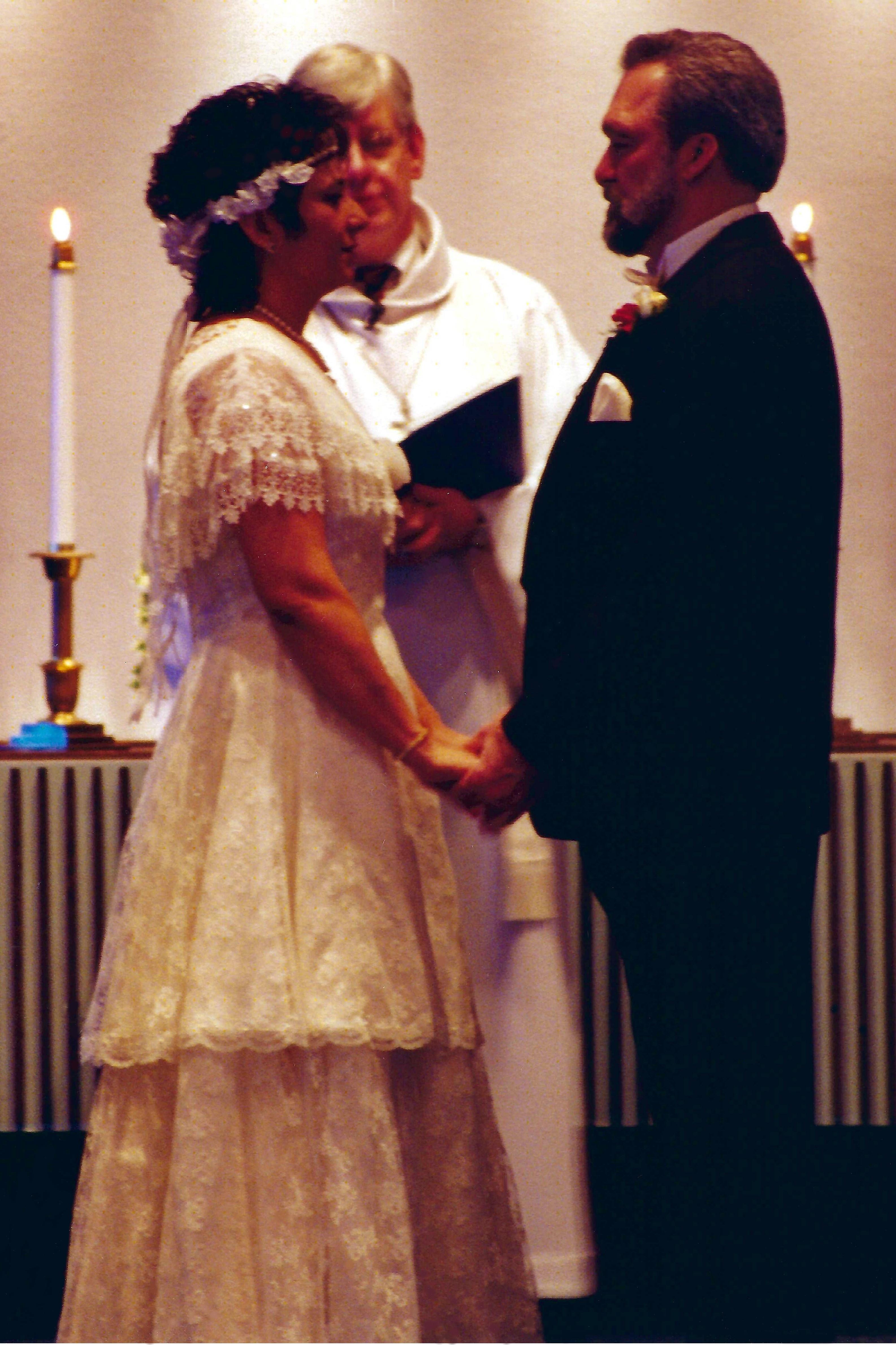 A couple stands hand in hand while exchanging vows in a decorated ceremony space.