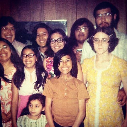 A cheerful family gathering in a cozy living room featuring several people in 1970s attire.
