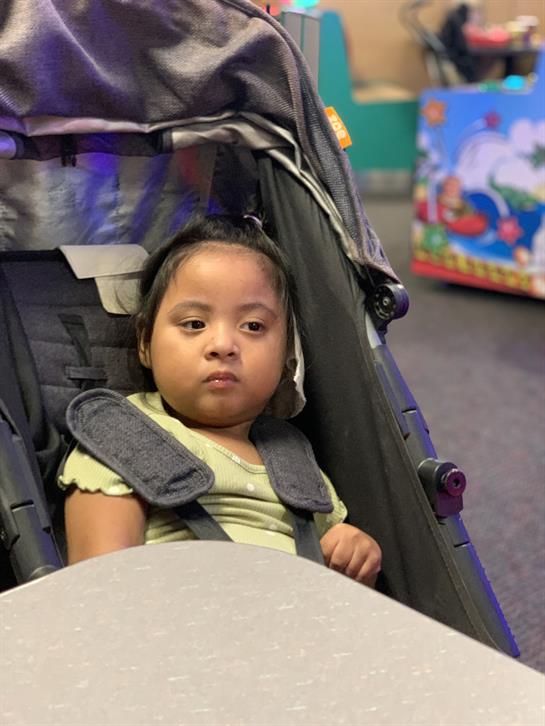A young girl in a green shirt looks contemplatively from her stroller in a lively play center.