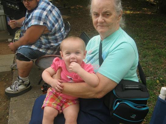 An elderly woman enjoys a moment with a baby on her lap in a park setting.