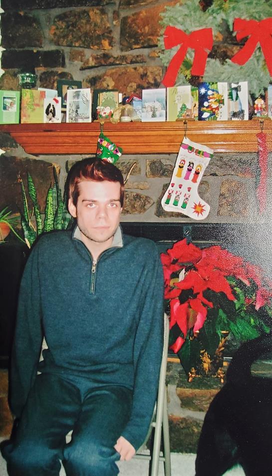 A young man sits on a chair in a decorated living room filled with holiday cheer.
