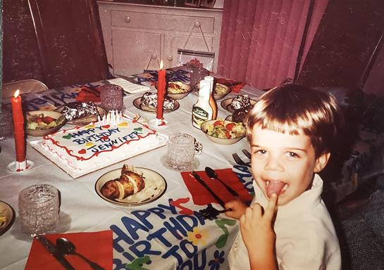 A boy joyfully enjoys his birthday party with cake, decorations, and a festive table setting.