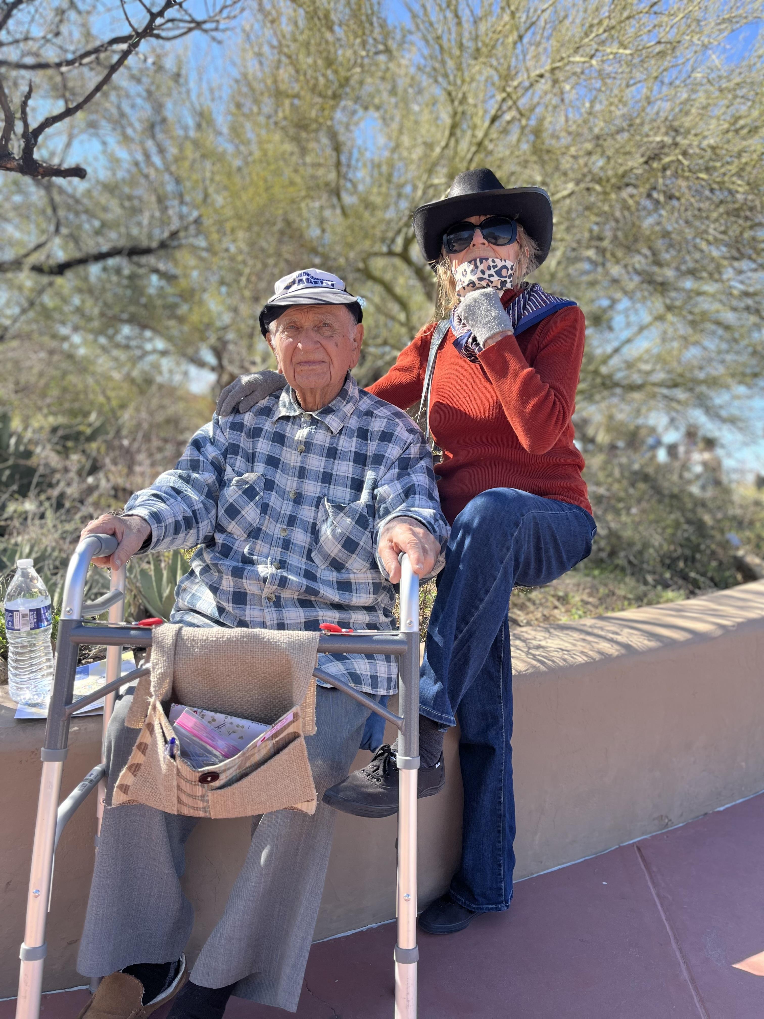 An elderly couple relaxes in a desert park, enjoying the sun in colorful outfits.