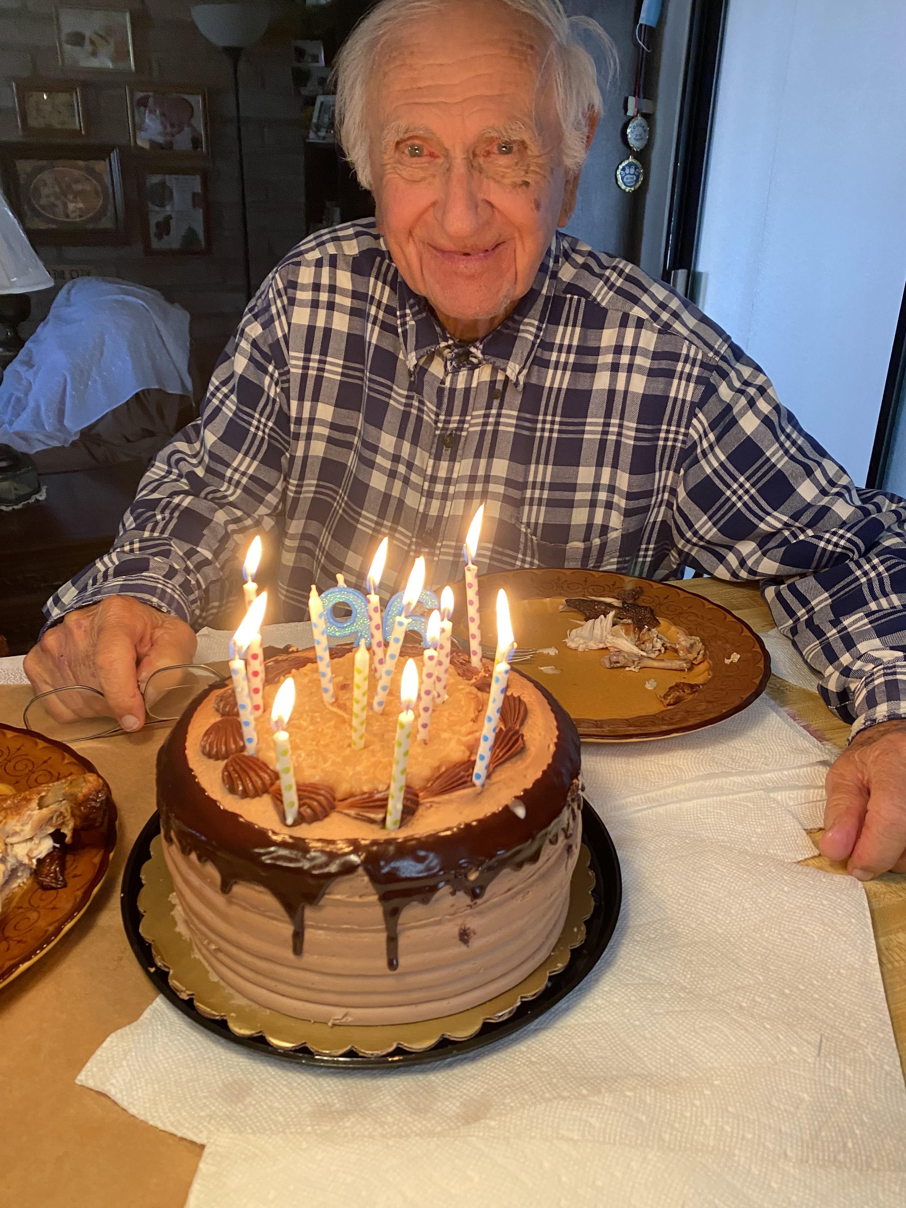 An elderly man enjoys his birthday cake adorned with candles, surrounded by loved ones.