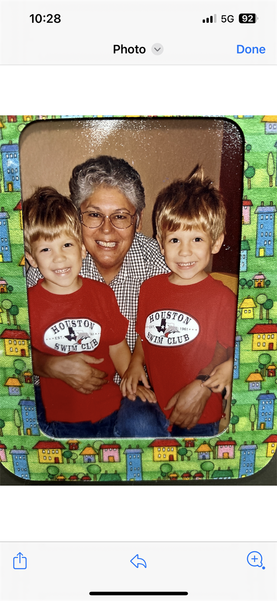 A grandmother enjoys a warm embrace with her twin grandsons, all smiling happily together.